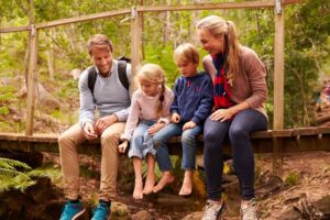 Family of four sitting on a wooden bridge in a New Zealand forest enjoying outdoor time together.