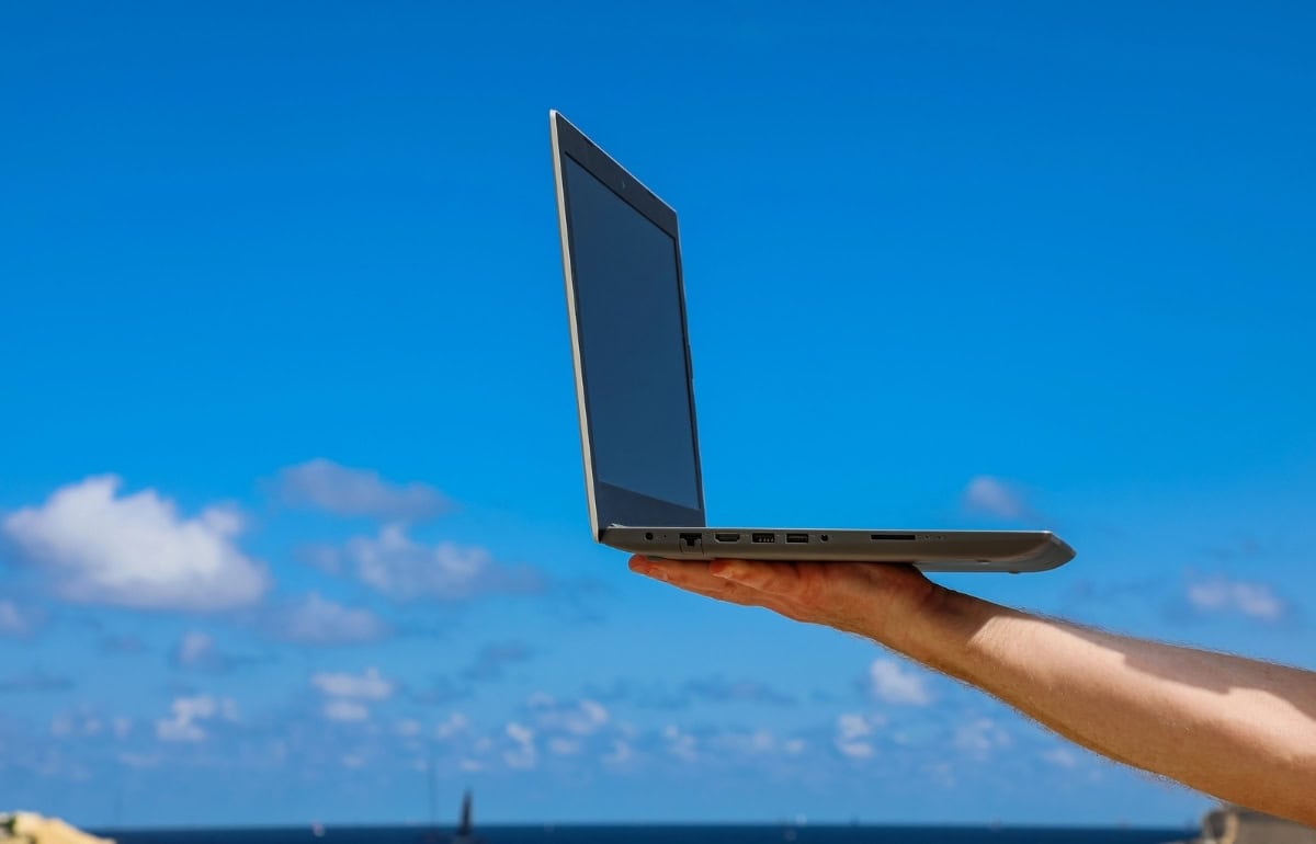 Person holding a laptop outdoors with the sea and blue sky in the background, symbolising remote work and job opportunities in Malta.